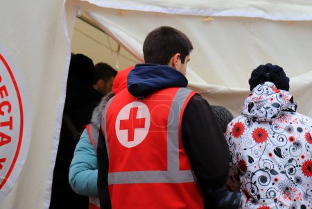 Téléchargez les photos : Dnipro Ukraine 2023-01-14. Red Cross volunteers help wounded near destroyed house after Russian missile attack. Red cross badge on uniform of paramedic - en image libre de droit