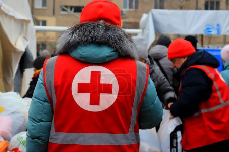 Foto de Dnipro Ukraine 2023-01-14. Red Cross volunteers help wounded near destroyed house after Russian missile attack. Red cross sign on uniform of paramedic - Imagen libre de derechos