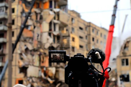 Foto de Camarógrafo filmando una casa destruida rota en Ucrania después del ataque con misiles rusos. La agencia de noticias transmite en vivo desde la escena de la explosión. City Dnipro. Rusia guerra contra Ucrania - Imagen libre de derechos
