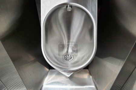 Photo for Sanitary metal urinal, toilet bowl in public bathroom with hygienic automatic water saving electronic flush. Urinal with urine sensor. Inductive flush toilet. WC, Modern plumbing - Royalty Free Image