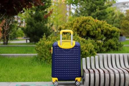 Téléchargez les photos : Valise de voyage jaune bleu sur roues dans le parc près de la gare routière, aéroport, voyage. Belle valise près de l'hôtel, auberge, maison d'hôtes, maison - en image libre de droit