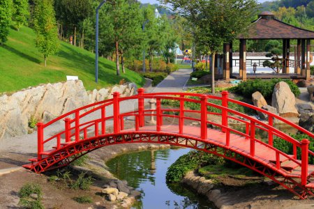 Old red wooden bridge across small river in park. Vintage Japanese style bridge, water. Uman park, Ukraine in summer, spring, autumn.