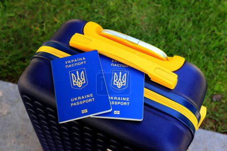 2 passports Ukraine citizens with inscription in Ukrainian - Passport of Ukraine lie on yellow blue suitcase in color of Ukrainian flag. Travel, refugees, tourism, emigration, mobilization, migrants