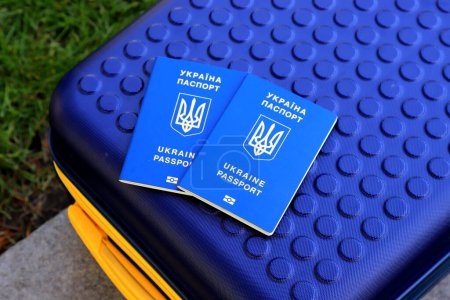 2 passports Ukraine citizens with inscription in Ukrainian - Passport of Ukraine lie on yellow blue suitcase in color of Ukrainian flag. Travel, refugees, tourism, emigration, mobilization, migrants