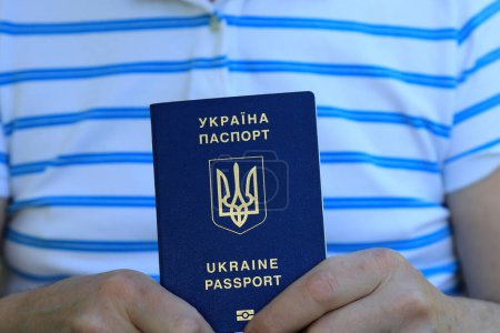 A man holds in his hands a Ukrainian passport with an inscription in Ukrainian - Passport of Ukraine. Travel concept, refugee, tourist, emigrant, mobilization, migrant.
