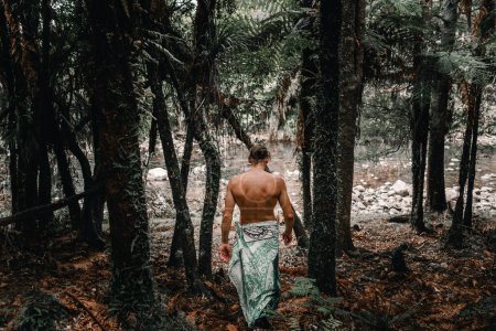Foto de De hombros anchos desnudo pecho caucásico joven camina hacia el río entre los árboles del bosque con las piernas envueltas en una toalla en el tranvía waitawheta, Nueva Zelanda - Concepto de estilo de vida - Imagen libre de derechos