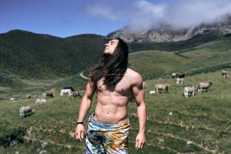 Téléchargez les photos : Jeune homme caucasien avec de longs cheveux lâches, torse nu avec un paréo autour de sa taille, les yeux fermés respirant l'air pur de la nature, ruta del cares asturias, espagne - Lieux traditionnels espagnols - en image libre de droit