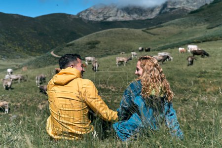 Téléchargez les photos : Caucasien garçon et fille assis à côté de l'autre sur l'herbe du champ en se regardant souriant en se tenant la main par une journée ensoleillée dans la nature, ruta del cares asturias, espagne - Espagnol traditionnel - en image libre de droit