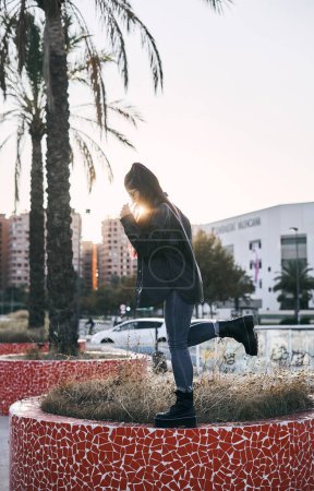Photo for Young latin brunette woman with long hair glasses blue pants standing on one leg in small garden next to palm trees in urban park - Urban concept - Royalty Free Image