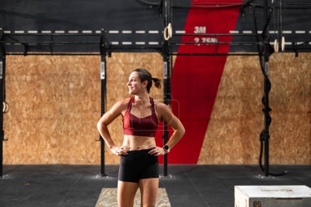 caucasian young woman doing sports with hands on waist resting smiling looking to the side - Crossfit concept