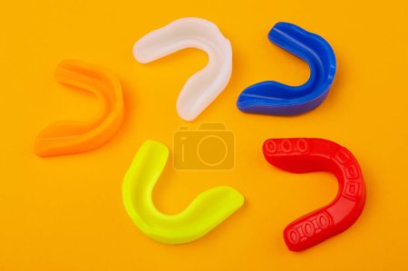 five boxing mouthguards of different colors lie on a yellow background, concept