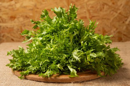 Foto de Large bunch of frisee lettuce on a round wooden board, selective focus - Imagen libre de derechos