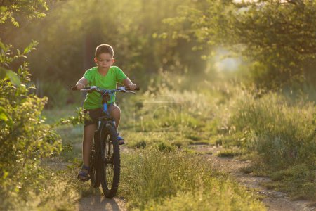 Foto de Boy rides a bike along a path surrounded by greenery, beautiful sunlight, copy space - Imagen libre de derechos