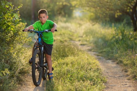 Foto de A boy in a green T-shirt starts cycling, in nature, surrounded by greenery, beautiful sunlight and bokeh - Imagen libre de derechos