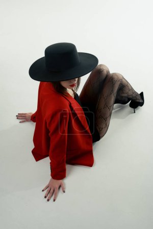 Téléchargez les photos : Young girl in a hat and a red jacket poses in the studio - en image libre de droit