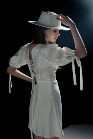 Téléchargez les photos : A young girl in a white hat and dress poses in the studio - en image libre de droit