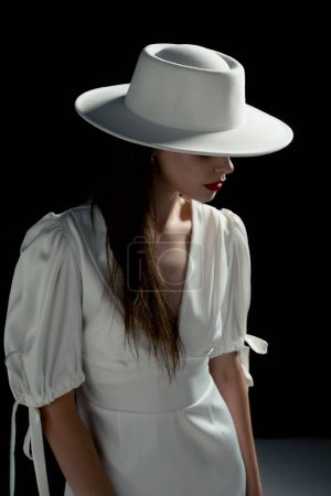 Photo for A young girl in a white hat and dress poses in the studio - Royalty Free Image