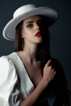 Foto de A young girl in a white hat and dress poses in the studio - Imagen libre de derechos