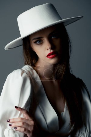 Foto de A young girl in a white hat and dress poses in the studio - Imagen libre de derechos