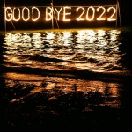 good bye 2022 burning phrase made of fire stick placed on water in sea, happy new year celebration in tropical place at night, inscription on the beach
