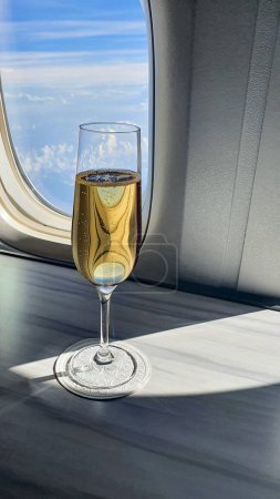 glass of champagne in flute on table in aircraft cabin near airplane window. Luxury travel concept, flying business class