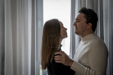 Photo for Romantic couple hugging each other near window at home, woman in black man in white, yin yang contrast, opposites attract. Love my second half - Royalty Free Image