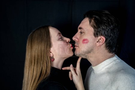 Photo for Couple on dark background, woman in black. Man in white, partners look at each other. Lipstick print on male cheek. Family, yin yang contrast, opposites attract. Girlfriend kissing boyfriend, passion - Royalty Free Image