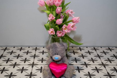 Foto de Peluche de peluche gris osito de peluche con corazón rosa junto al ramo de flores de tulipanes en florero rosa. Feliz regalo de San Valentín - Imagen libre de derechos