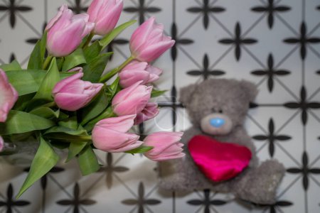 Foto de Peluche de peluche gris osito de peluche con corazón rosa junto al ramo de flores de tulipanes en florero rosa. Feliz regalo de San Valentín - Imagen libre de derechos