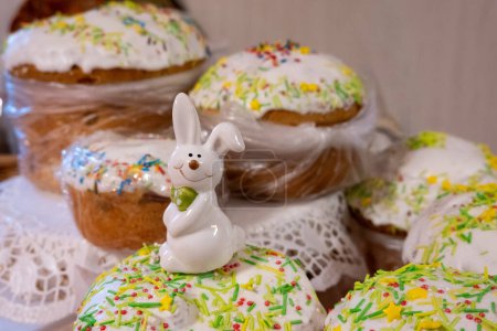 Photo for White easter rabbit standing on home-baked easter cakes with icing on a table in the kitchen. Religious holiday - Royalty Free Image