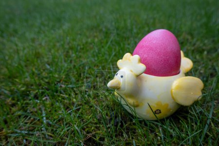 huevo de Pascua de color rosa en el soporte de cerámica en forma de pollo sobre fondo verde. Feliz Pascua. Ha resucitado. 