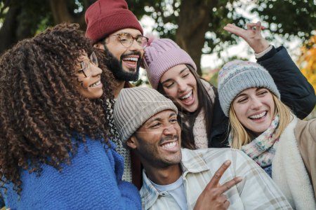 Foto de Close up portrait of a group of young people faces, smiling and having fun together. Multiracial happy friends with hats, coats and autumnal clothes enjoying a weekend day. Lifestyle concept. High - Imagen libre de derechos
