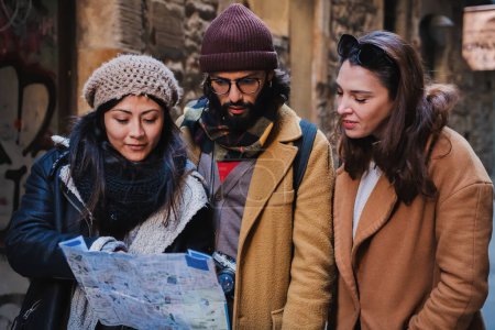 Téléchargez les photos : Group of multiracial tourist friends looking and searching directions on a map or guide, ejoying the trip visiting a city on vacations. Travel concept. High quality photo - en image libre de droit
