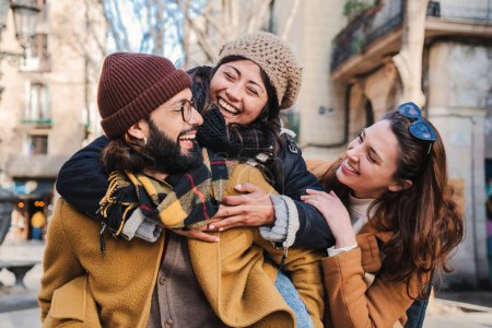Photo for Multiracial group of three happy friends having fun and laughing together. Bearded male giving his girlfriend a piggyback ride. Tourist hugging each other and enjoying a travel trip in Europe. High - Royalty Free Image