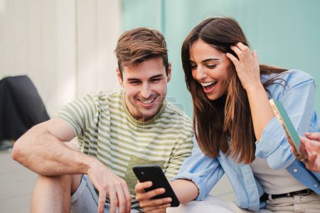 Photo for Two teenage happy friends watching funny videos browsing on internet app with a smartphone and smiling together. Caucasian couple using a cell phone to post in a social media and chatting online. High - Royalty Free Image