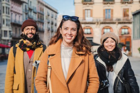 Téléchargez les photos : Groupe de jeunes regardant la caméra sur la rue européenne de la ville. Portrait de trois amis multiethniques joyeux debout à l'extérieur lors d'un voyage. Vue de face de quelques hipsters heureux appréciant ensemble. Haut - en image libre de droit