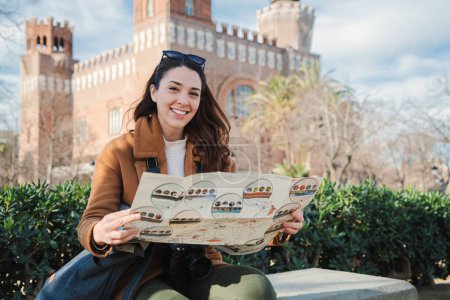 Photo for International tourist woman searching a location on a map. Happy female traveler smiling and looking at camera holding a guide on a europe journey. Lady on a historic tour visiting a monument. trip - Royalty Free Image