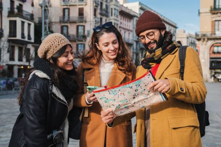 Foto de Grupo de turistas leyendo un mapa para fundar la ubicación de un monumento europeo. Tres jóvenes viajeros observando a un guía que busca indicaciones para visitar la ciudad de Barcelona en un viaje. Amigos turismo - Imagen libre de derechos