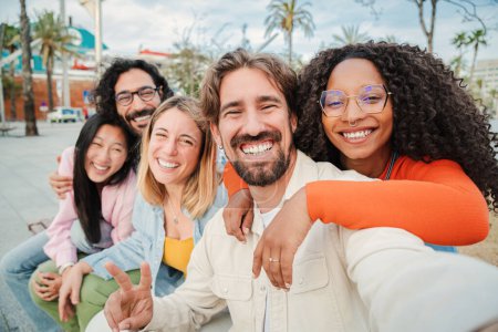 Téléchargez les photos : Groupe d'amis multiraciaux souriant et prenant un portrait selfie. Les jeunes s'amusent lors d'un rassemblement social. Joyeuse équipe de jeunes heureux tirant sur un foto de soi avec un téléphone portable sur une réunion - en image libre de droit