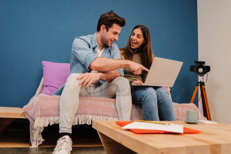 Photo for Caucasian american young couple using a laptop to rent a new home. Cherful wife and handsome husband searching on internet a new apartment together sitting at couch. People browsing with a computer - Royalty Free Image