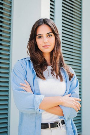 Photo for Vertical portrait of a pensive teenage woman with confident face expression posing. Caucasian serious young female student with arms crossed looking pensive at camera in casual clothes outdoors - Royalty Free Image