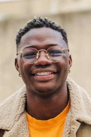 Photo for Vertical close up portrait of african american teenage boy looking at camera smiling and laughing at univesity campus. Smart young student standing outdoors at college with backpack and googles. High - Royalty Free Image