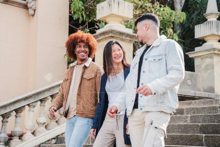 Photo for Group of teenage students walking down stairs, talking and smiling at university campus. Three multiracial young friends sightseeing and having fun together. Cheerful people emjpying the weekend. High - Royalty Free Image