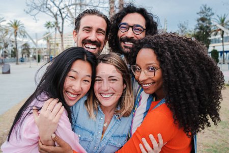 Photo for Group of joyful young adult friends hugging each others. Happy smiling multiracial people having fun embracing and laughing together on a social gathering. Community, union and friendship concept - Royalty Free Image