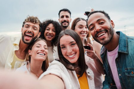 Foto de Gran grupo de jóvenes adultos felices amigos sonriendo tomando un retrato selfie y mirando a la cámara con expresión amistosa. Mucha gente alegre y multirracial celebrando y riendo. Buddies vinculación - Imagen libre de derechos
