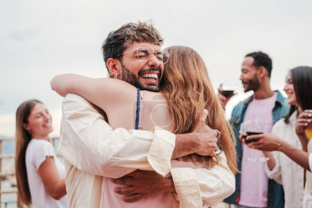 Photo for Happy man and excited woman hugging at a party with a group of people at friendly meeting. Thankful guy embracing his female best friend. Male giving a grateful affectionate greeting. Couple bonding - Royalty Free Image