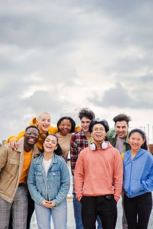Photo for Vertical portrait of a big goup of multiracial teenage highschool students having fun,smiling and laughing together. Young cool best friends cheering and enjoying a social gathering staring front - Royalty Free Image