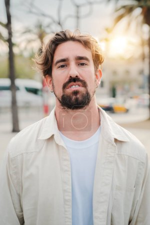 Photo for Vertical individual portrait of handsome bearded man looking serious at camera with pensive expression. Headshot of a cool guy staring front with success attitude. One guy standing thoughtful outside - Royalty Free Image