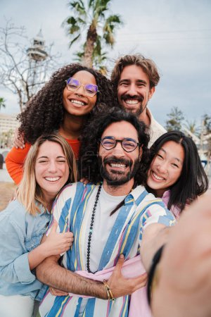 Foto de Vertical. Grupo de jóvenes adultos multirraciales sonriendo tomando una selfie juntos para compartir en la aplicación de redes sociales. Primer plano retrato de felices mejores amigos riendo y divirtiéndose en una reunión divertida - Imagen libre de derechos