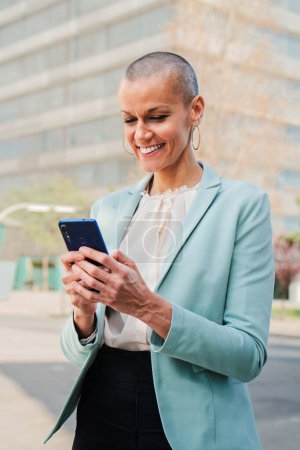Photo for Vertical portrait of a smiling business woman using a mobile phone to browse on internet and share on the social media. Corporate female worker watching successful her stock shares on cellphone app - Royalty Free Image
